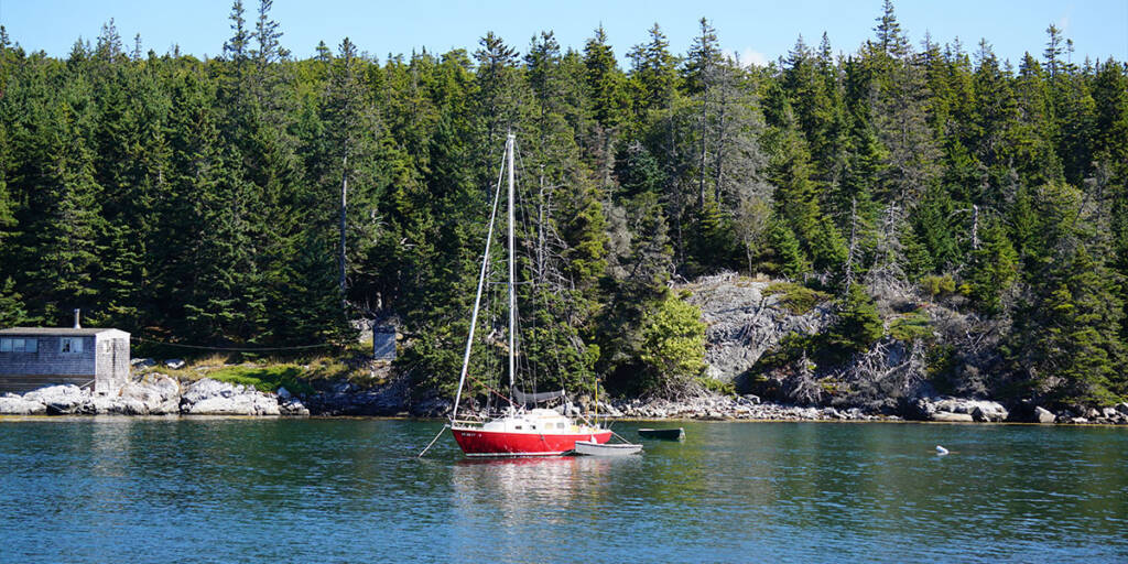 Red sailboat anchored near a forested shore, ideal for travelers using an RV Wi-Fi router.