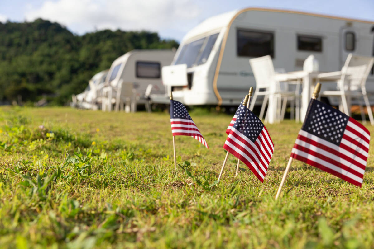 RV campgrounds with American flags near white caravans in a grassy area.