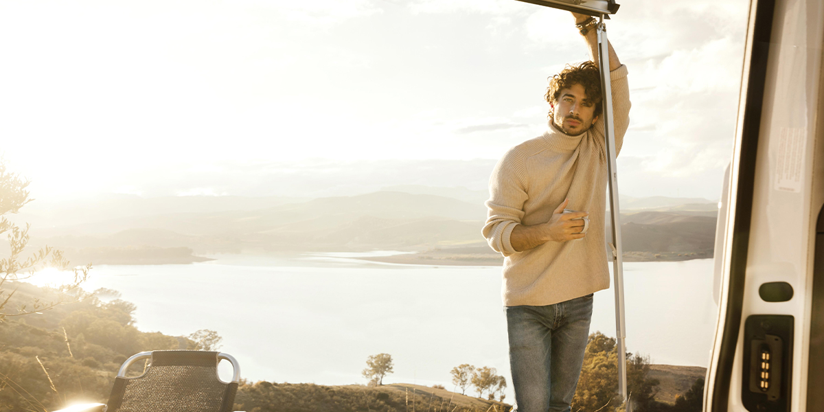 Person standing at the doorway of an RV, looking out at a scenic morning landscape — representing a moment of peaceful RV travel.