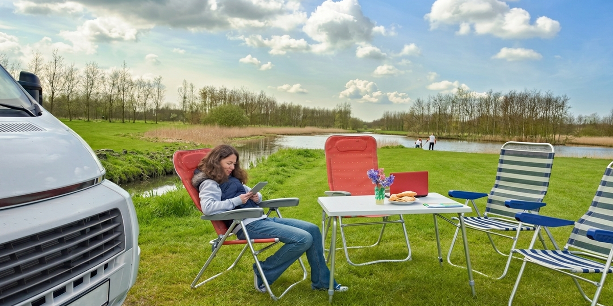 Using a tablet outdoors by a lake with a high-speed RV internet setup providing seamless connectivity at camp.