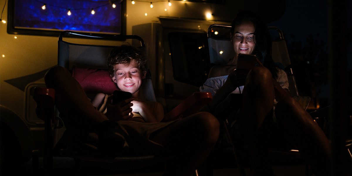 A couple enjoying an outdoor movie night at a campground streamed from their RV router's USB media server.