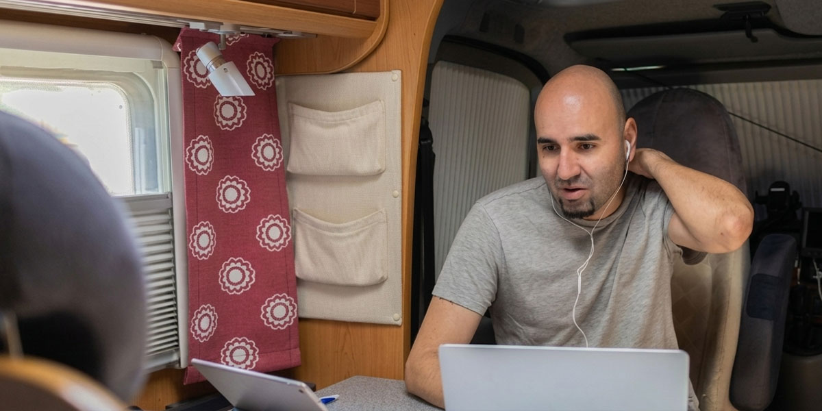 A remote worker using a laptop inside an RV parked at a scenic site, relying on a layered internet setup.