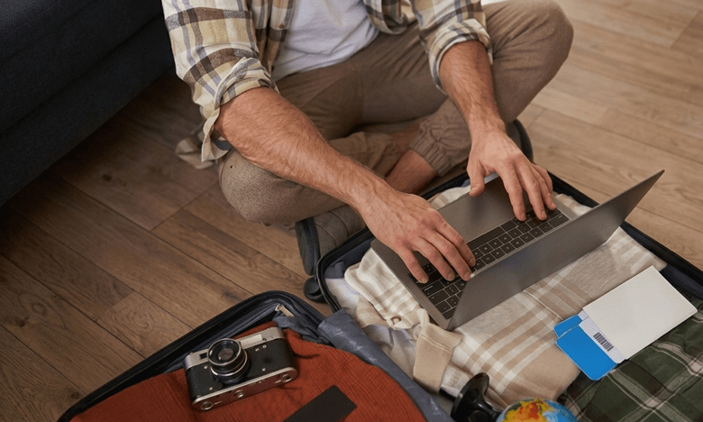An RV traveler packing a suitcase while downloading offline maps and travel documents on a laptop before departure.
