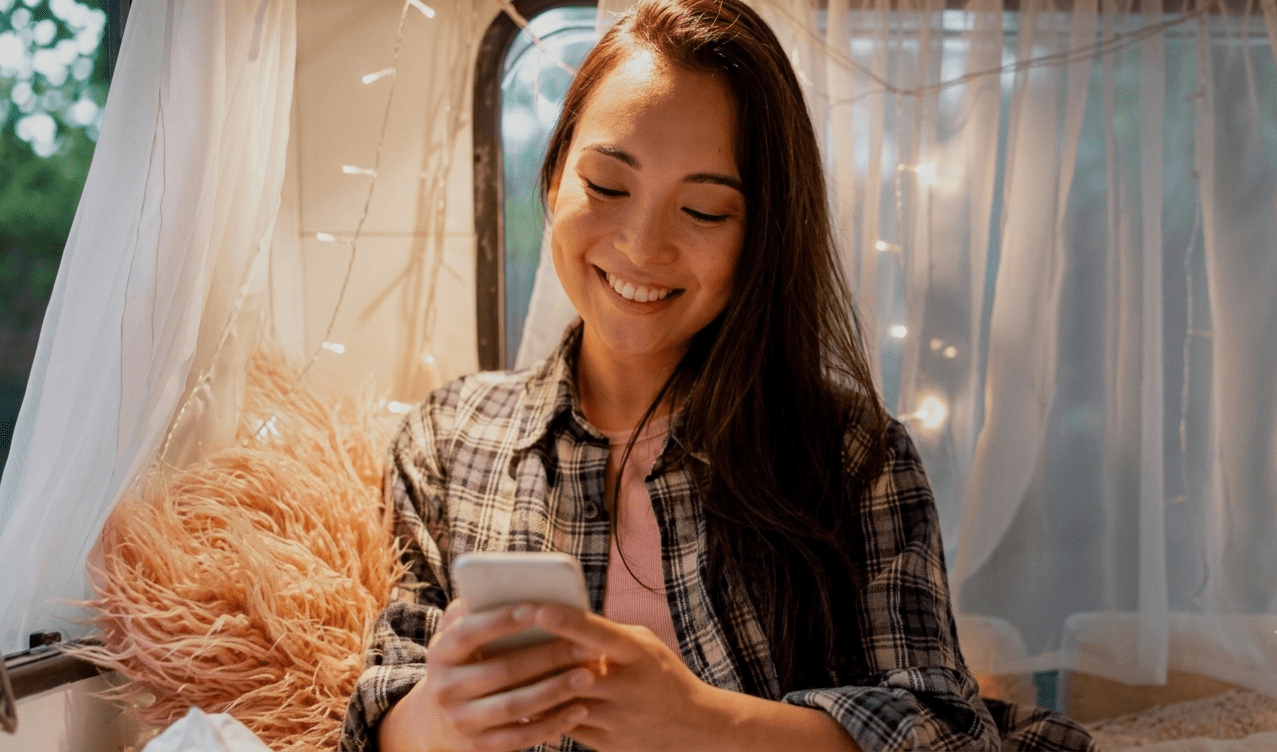 An RVer smiling at her phone inside a camper while sharing her trip location with family.