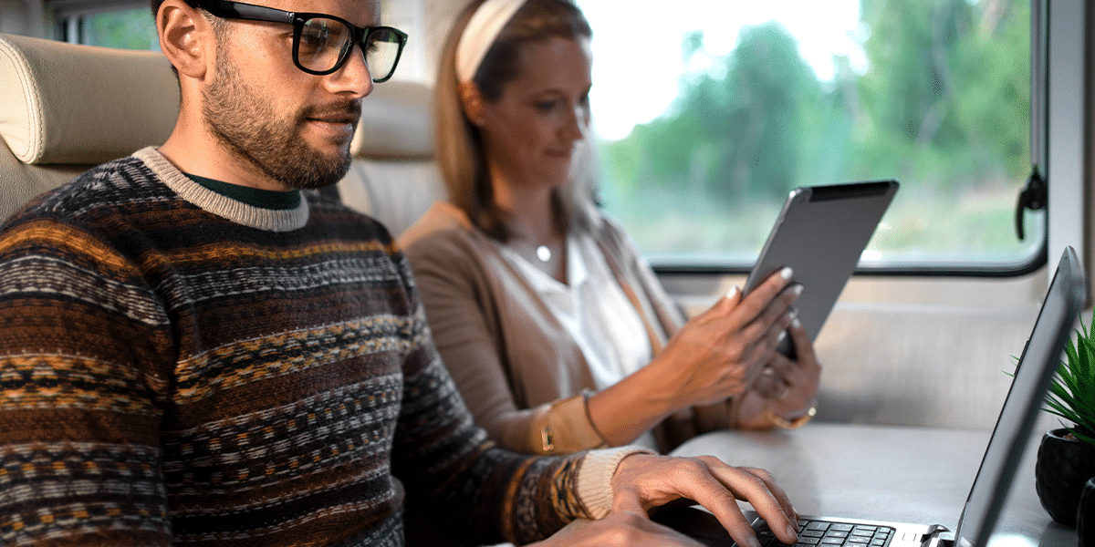 A man on a laptop and a woman on a tablet working online together inside an RV
